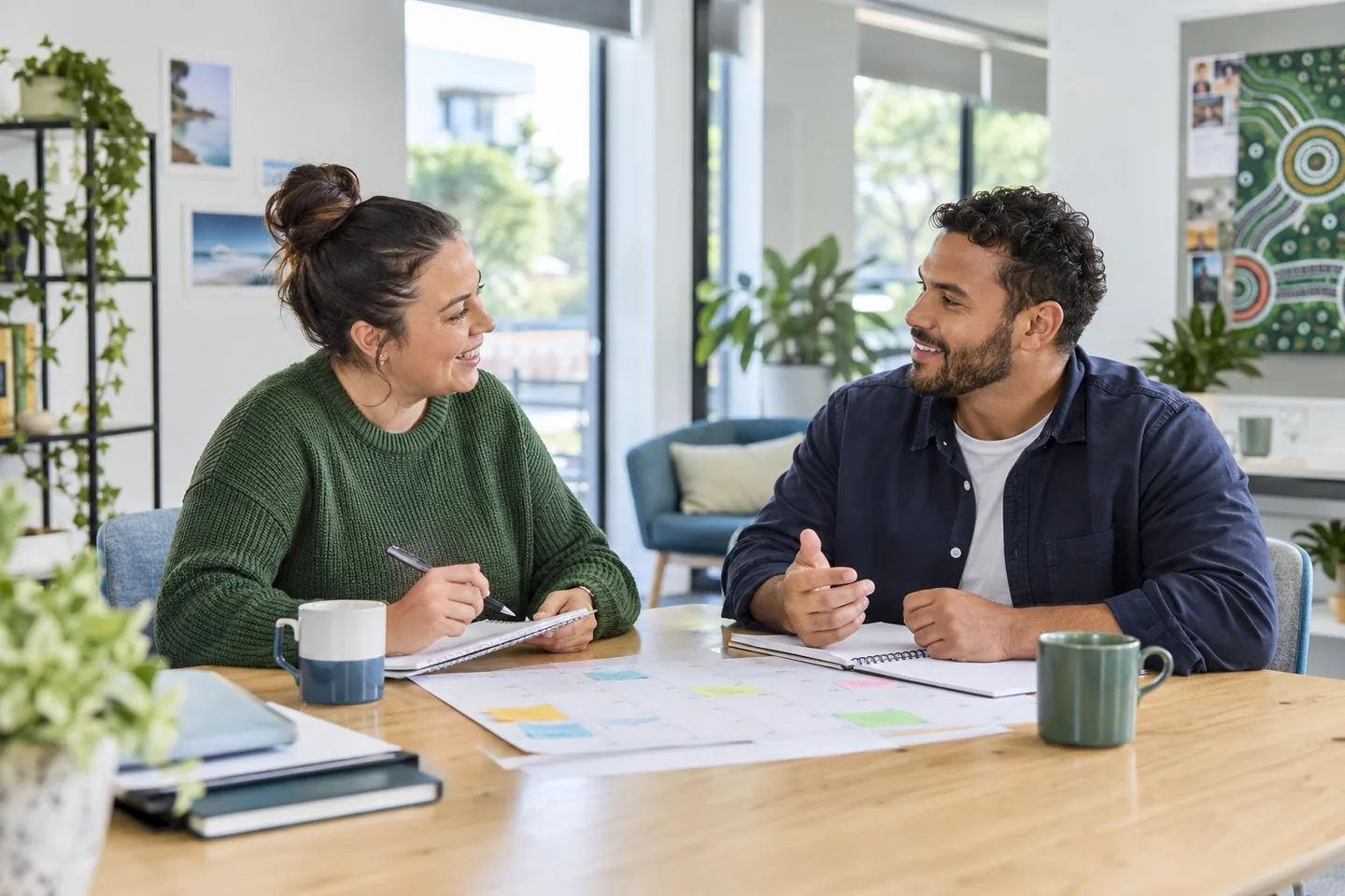 Two support workers planning their week together at a table in a bright community office